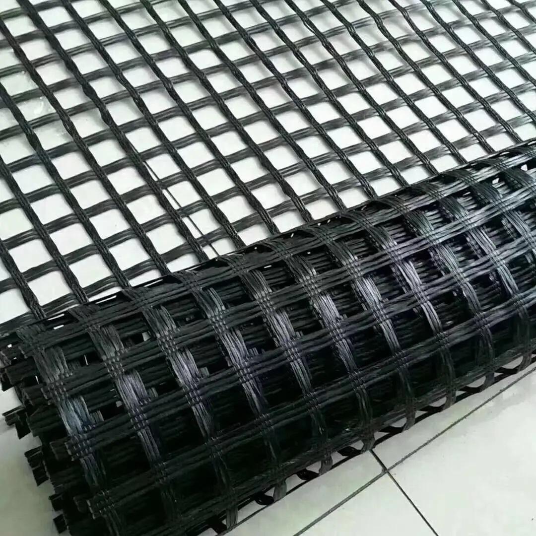 土工格栅产品展示，黑色网格状材料，平整铺设在地面上，阳光照射下清晰显示其结构